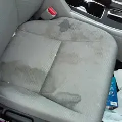 Grey cloth seat with dark stains before cleaning